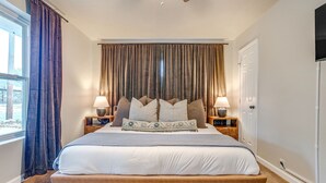 Un dormitorio con una cama grande, dos mesitas de noche con lámparas, un ventilador de techo y una ventana con cortinas.