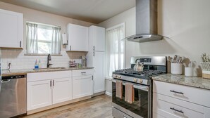 Una cocina moderna con gabinetes blancos, un lavavajillas de acero inoxidable, una estufa a gas y una campana extractora.