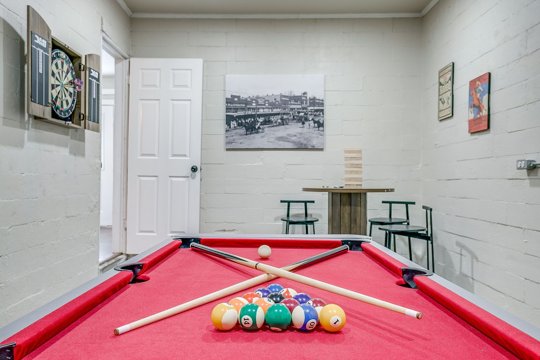 A pool table with balls and cues, a dartboard, and a framed picture on the wall.