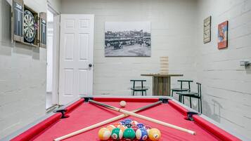 A pool table with balls and cues, a dartboard, and a framed picture on the wall.