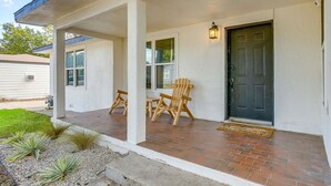 Una casa con porche, dos sillas de madera, una puerta negra y un pequeño jardín con plantas.