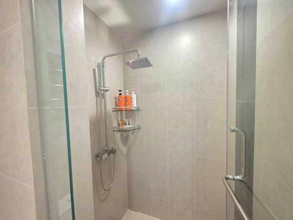 Ducha envuelta en vidrio con cabezal de ducha de mano y llave instalada en la pared. Hay tres estantes con artículos de aseo.