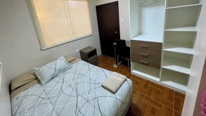 Un dormitorio con cama, armario, escritorio y ventana.