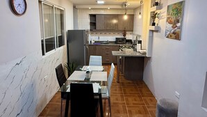 Cocina compacta con refrigerador, estufa y comedor con mesa y sillas.
