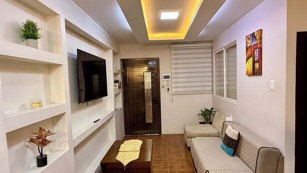 Una sala de estar moderna con un televisor de pantalla plana, estanterías empotradas, un sofá y piso de madera.