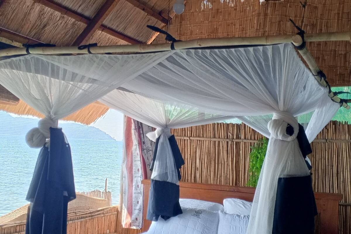 A bed with a canopy, a view of the sea, and a bamboo wall.