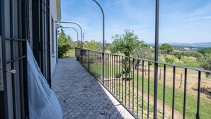 Ein Balkon mit Metallgeländer, der auf eine grüne Landschaft mit Bäumen und ferne Hügel blickt.