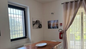 Ein Essbereich mit Holztisch, weißen Stühlen, einem Fenster mit Aussicht und einem Feuerlöscher an der Wand.