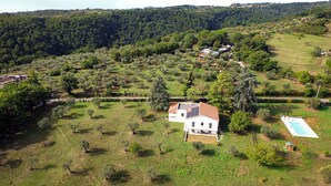 Ein großes Haus mit Schwimmbad, umgeben von üppiger, grüner Landschaft und Hügeln im Hintergrund.