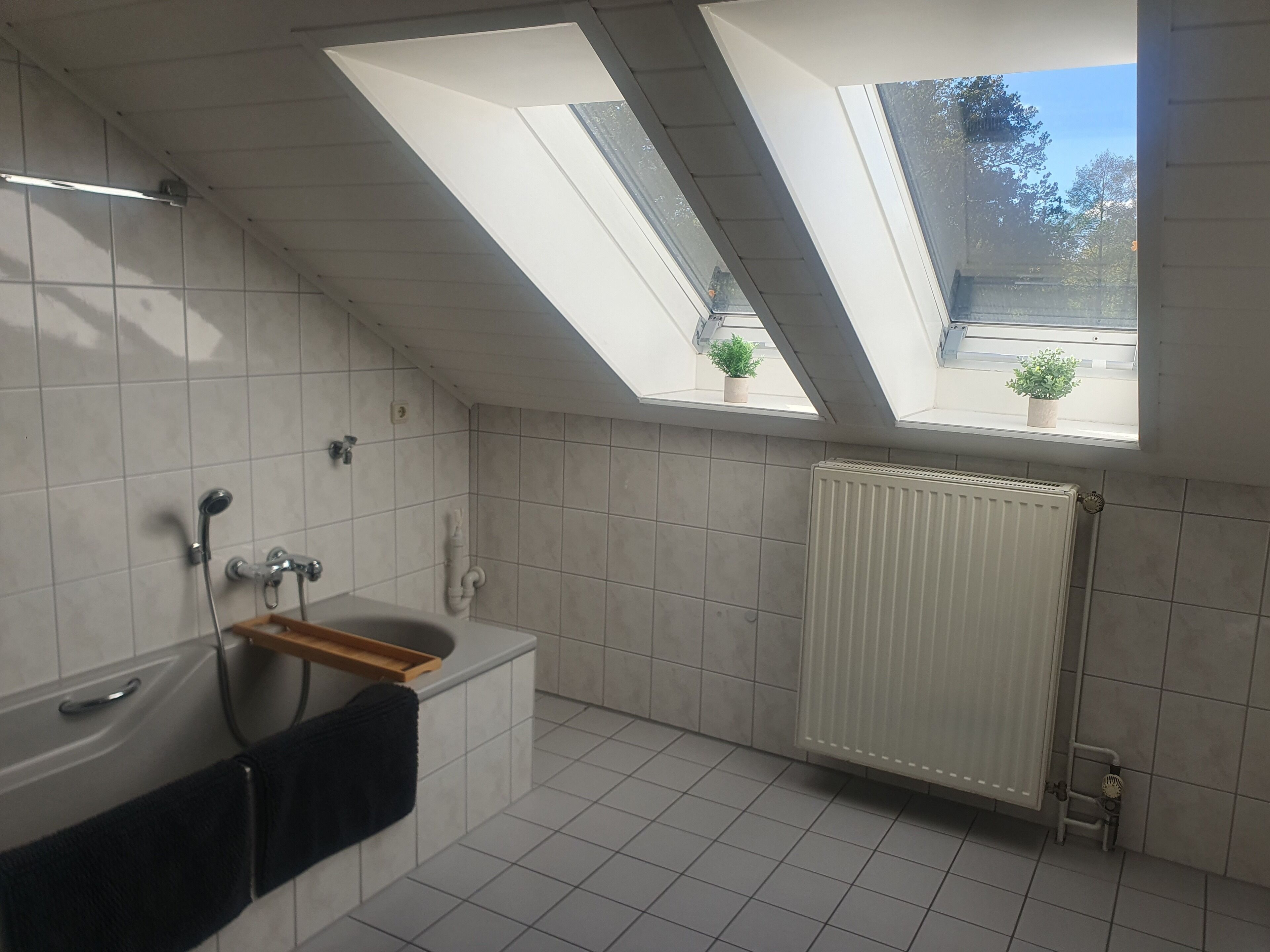 A modern bathroom with skylights, a bathtub, a shower, and a radiator.