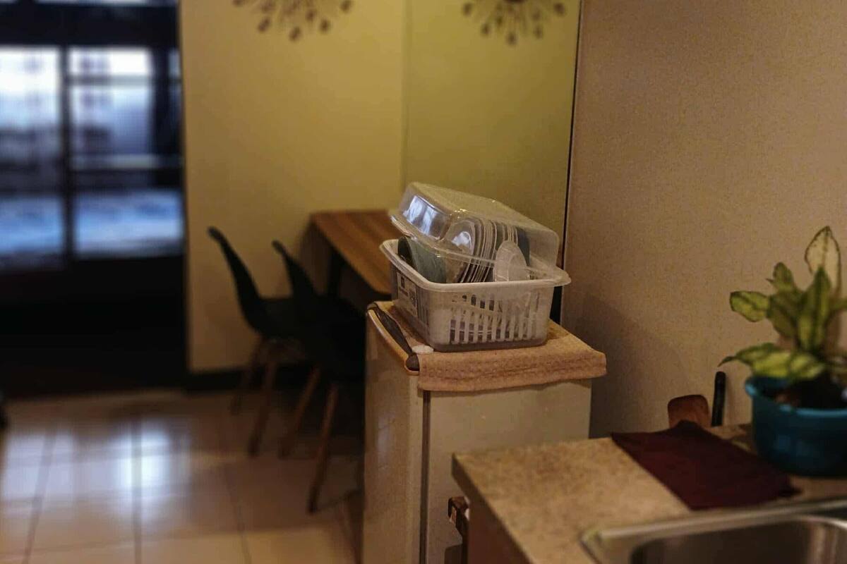 Une cuisine avec un évier, un plan de travail, un panier rempli de vaisselle, une plante et une horloge murale.