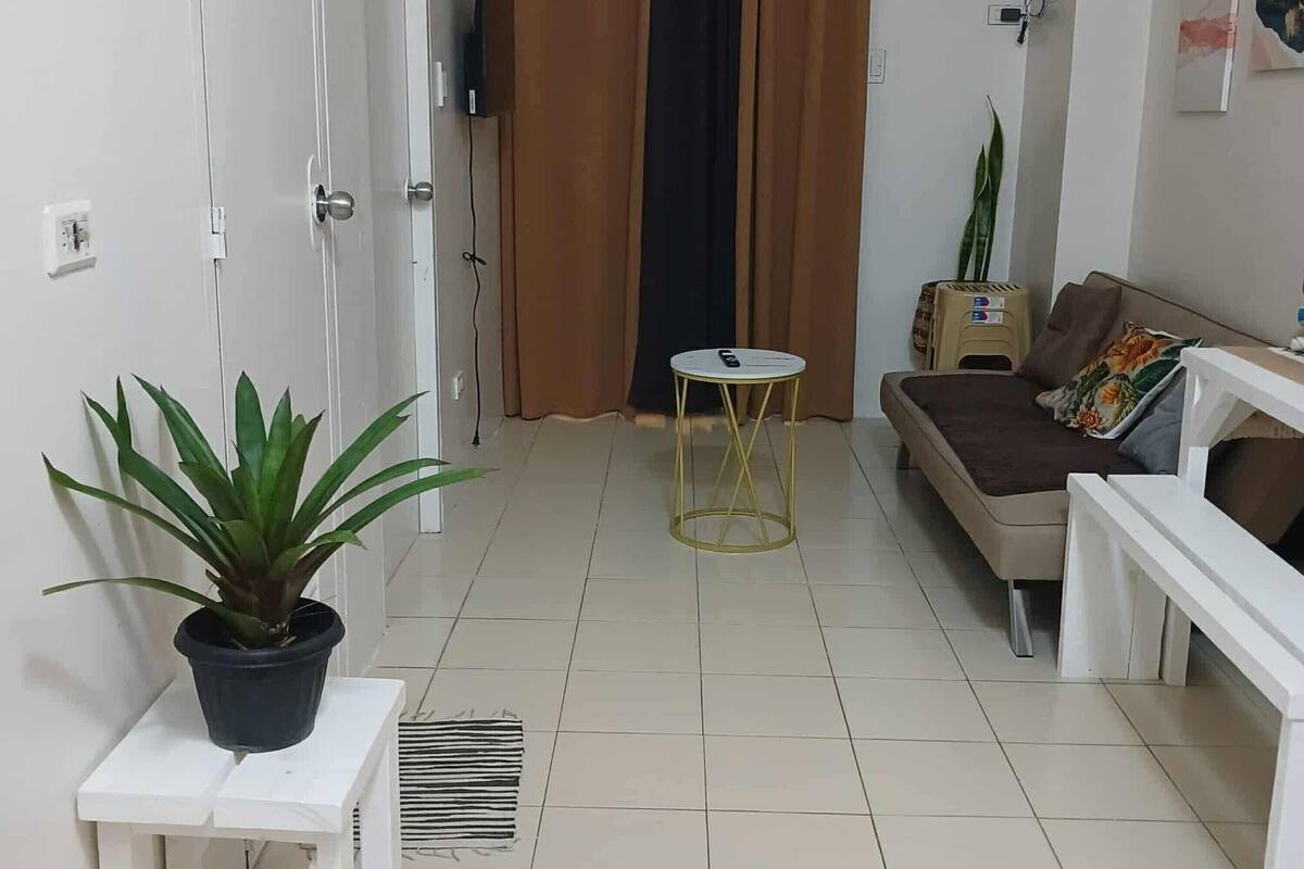 Un salon avec un canapé, une petite table, une plante en pot et un téléviseur.