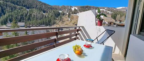 A balcony with a table, chairs, and a potted plant.