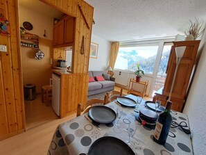 A cozy wooden cabin with a dining area, a sofa, and a window with a mountain view. - Mountain studio with balcony, small pets allowed (Pra-Loup)