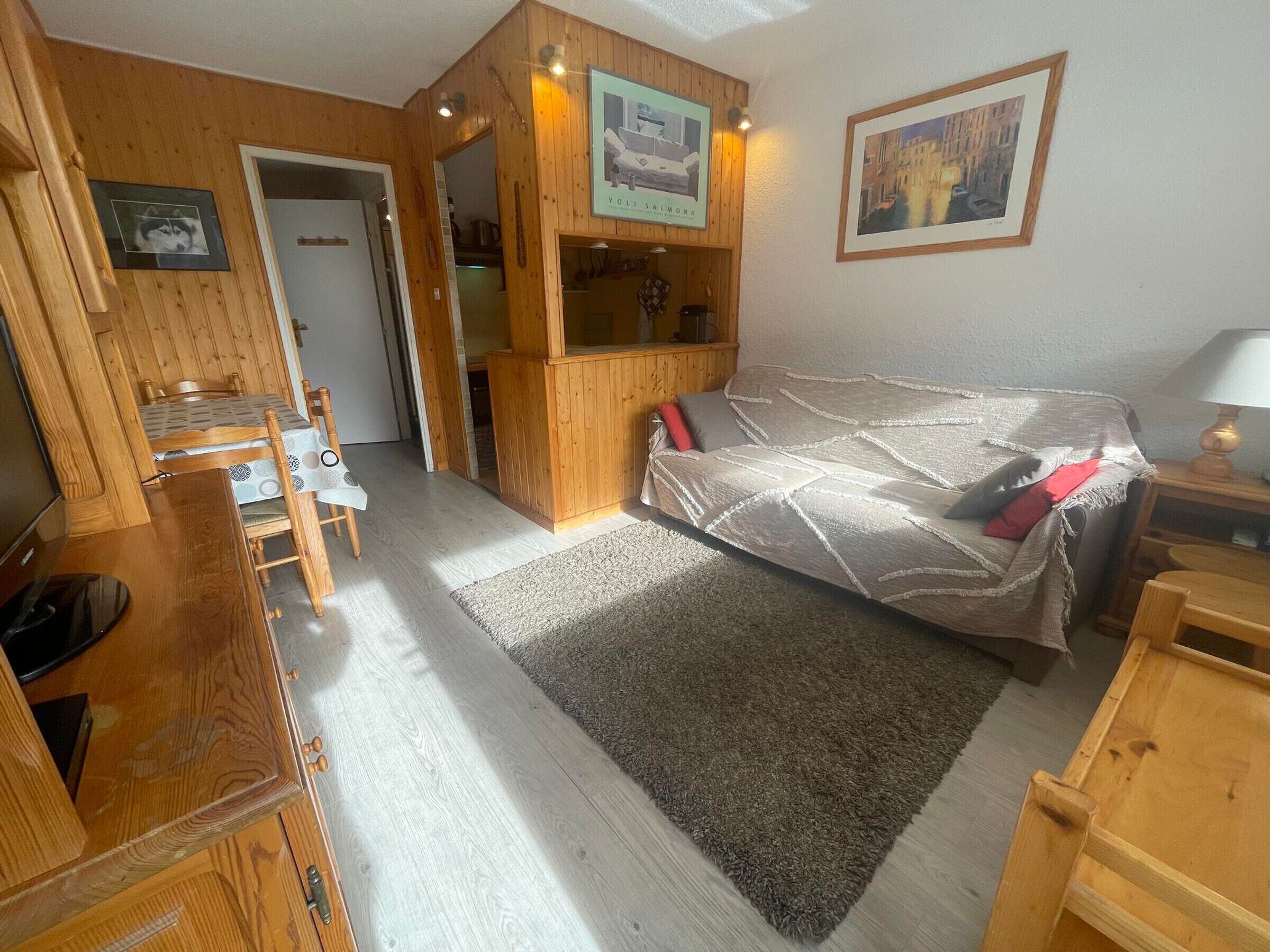 A compact living space with a sofa, a small table, and a TV. There is a wooden cabinet and a framed picture on the wall.