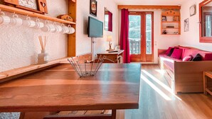 A cozy living room with a wooden table, a TV mounted on the wall, and a red curtain.