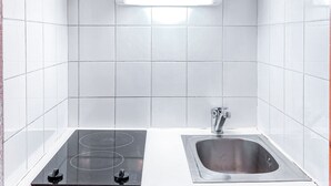 A kitchen with white tiles, a stainless steel sink, and a black induction cooktop.