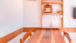 A wooden dining table with chairs, a wall-mounted shelf with decorative items, and a wall clock.