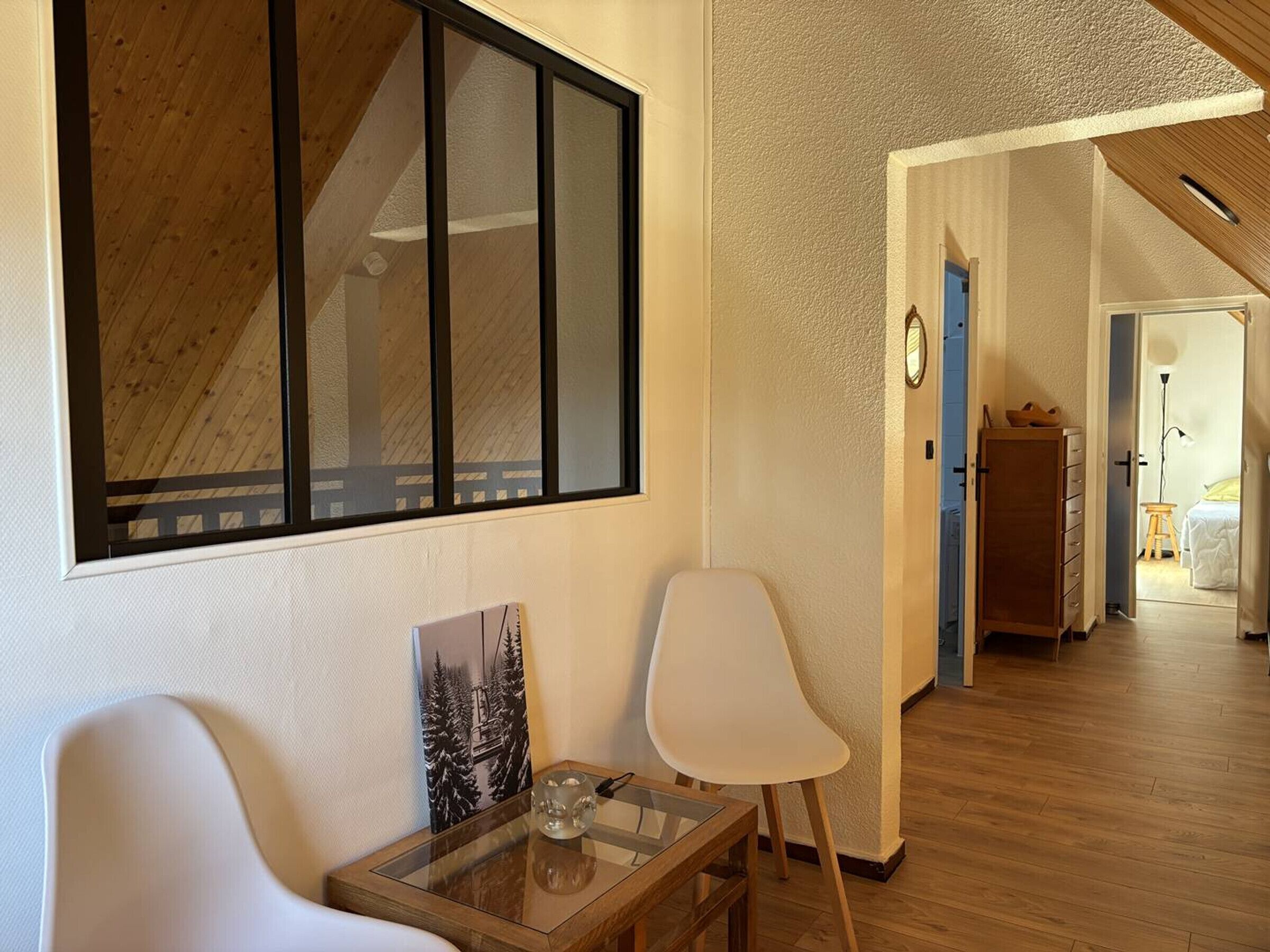 A modern interior with a large window, a wooden ceiling, and a hallway leading to a bedroom.
