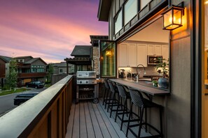 A modern outdoor kitchen with a grill, bar stools, and a view of neighboring houses.