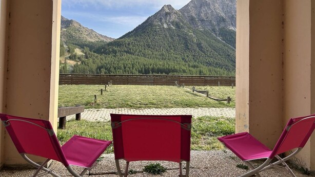 A balcony with two red chairs facing a mountain view.