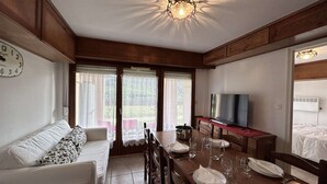 A cozy room with a sofa, dining table set for four, a TV, and a large window with curtains.