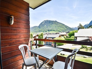 Ein Holzbalkon mit Tisch und zwei Stühlen, mit Blick auf eine Berglandschaft und ein Dorf.