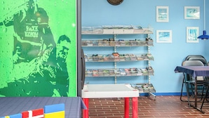 A room with a blue wall, a shelf with magazines, a table with a tablecloth, and a flag display.