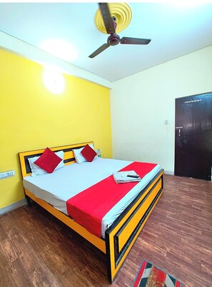 A single bed with a red and white bedspread, a ceiling fan, and a wooden floor. - Hotel Varanasi Paradise  (Varanasi)