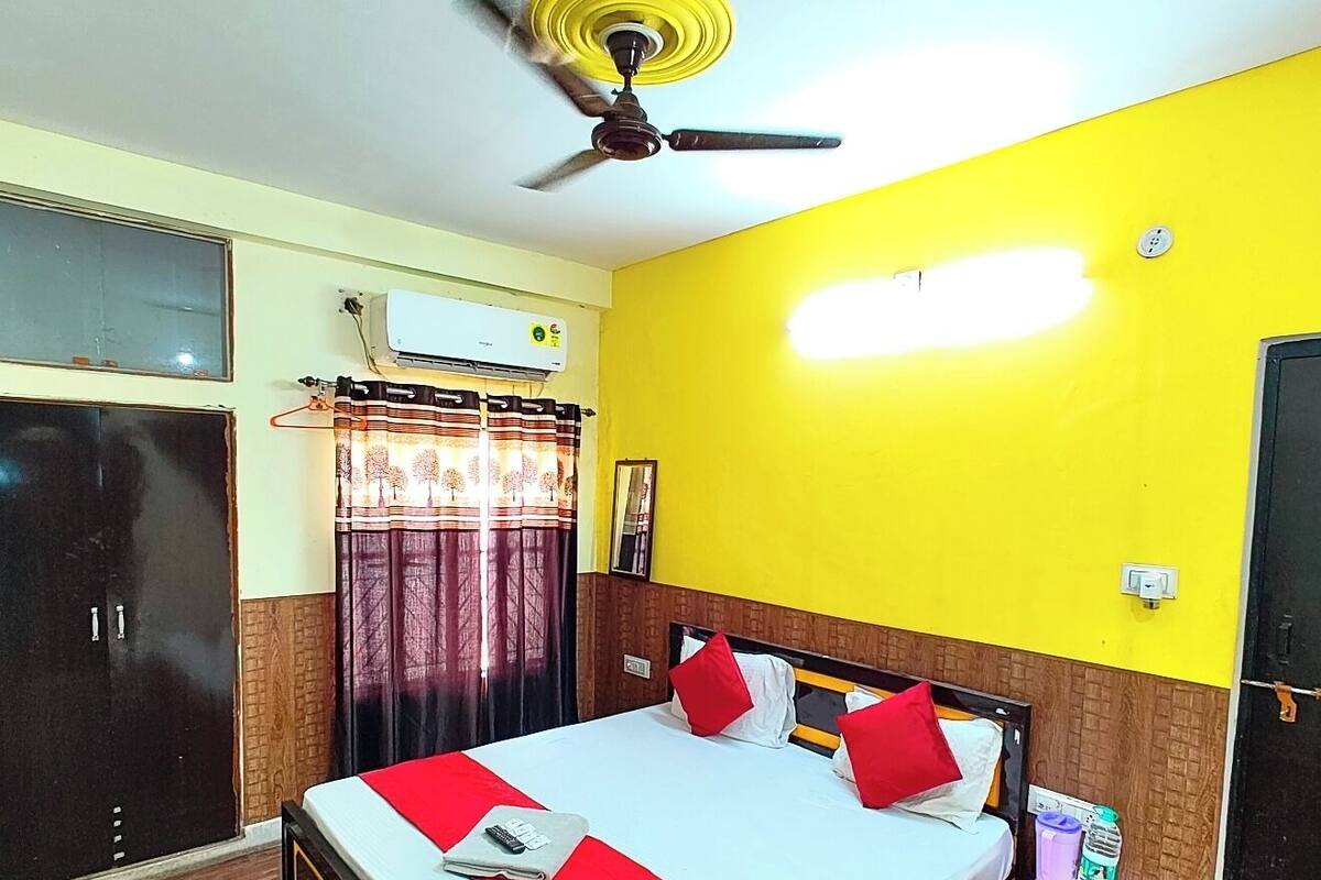 A hotel room with a bed, a wardrobe, a ceiling fan, an air conditioning unit, and a window with curtains.
