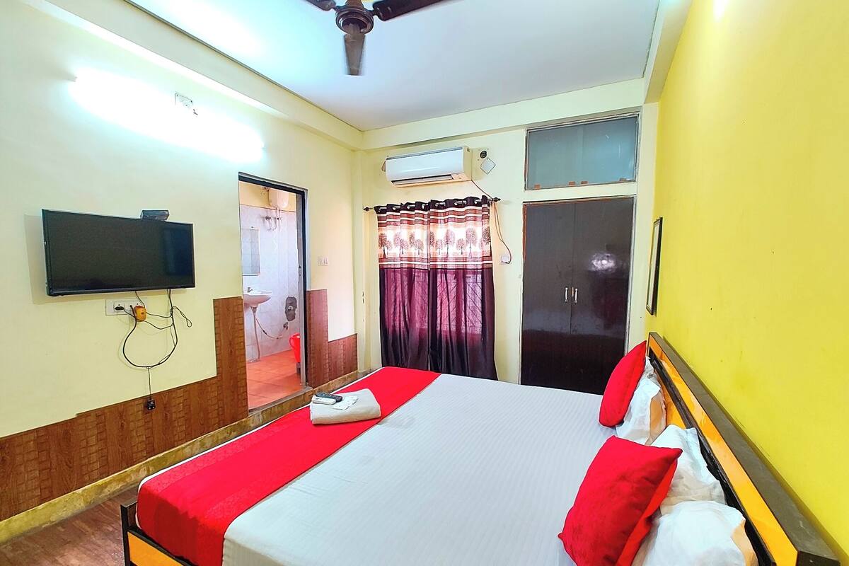 A hotel room with a bed, a television mounted on the wall, an air conditioning unit, and a wardrobe.