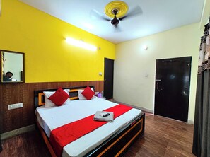 A hotel room with a bed, a ceiling fan, a mirror, and a door. - Hotel Varanasi Paradise  (Varanasi)