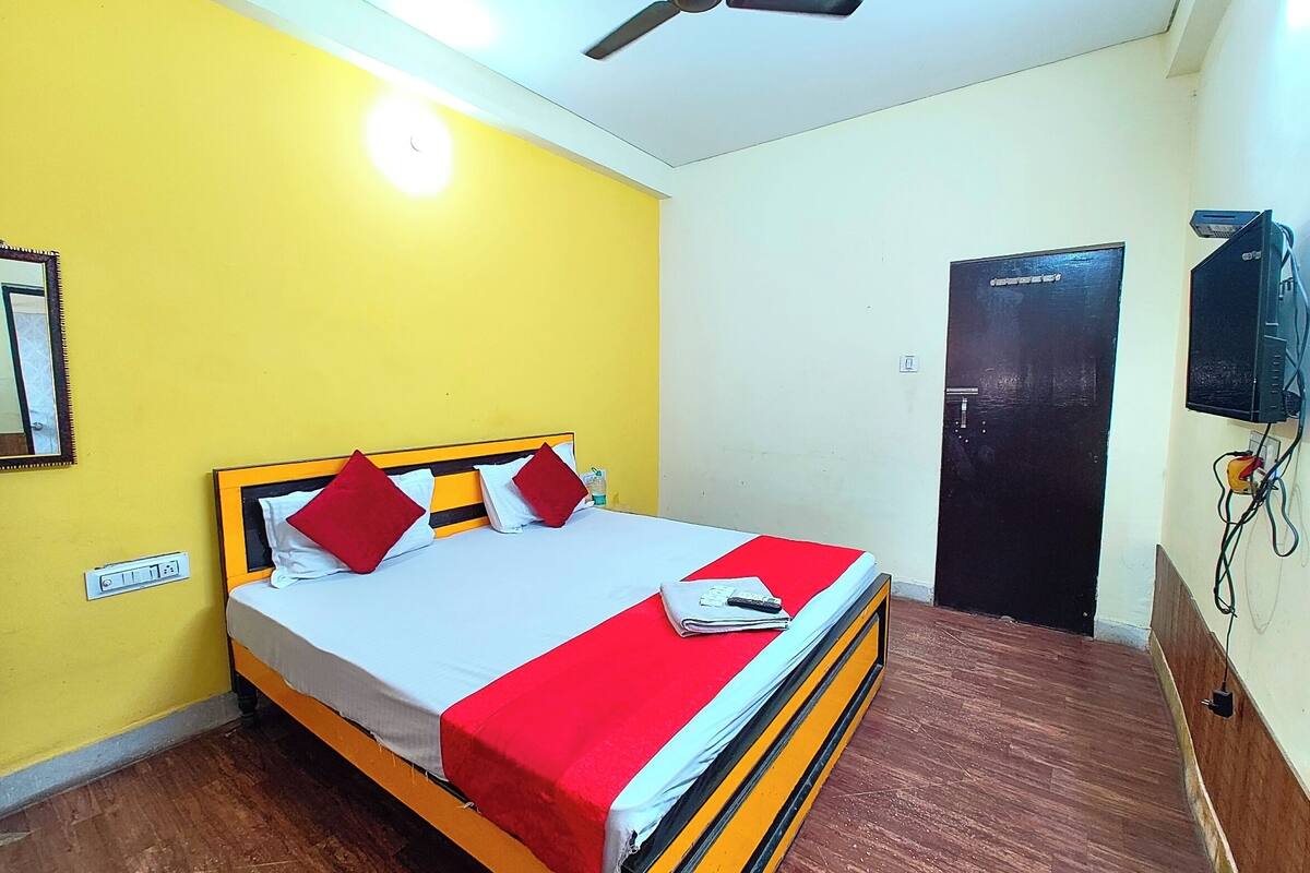 A room with a bed, a ceiling fan, a door, and a wall-mounted TV.