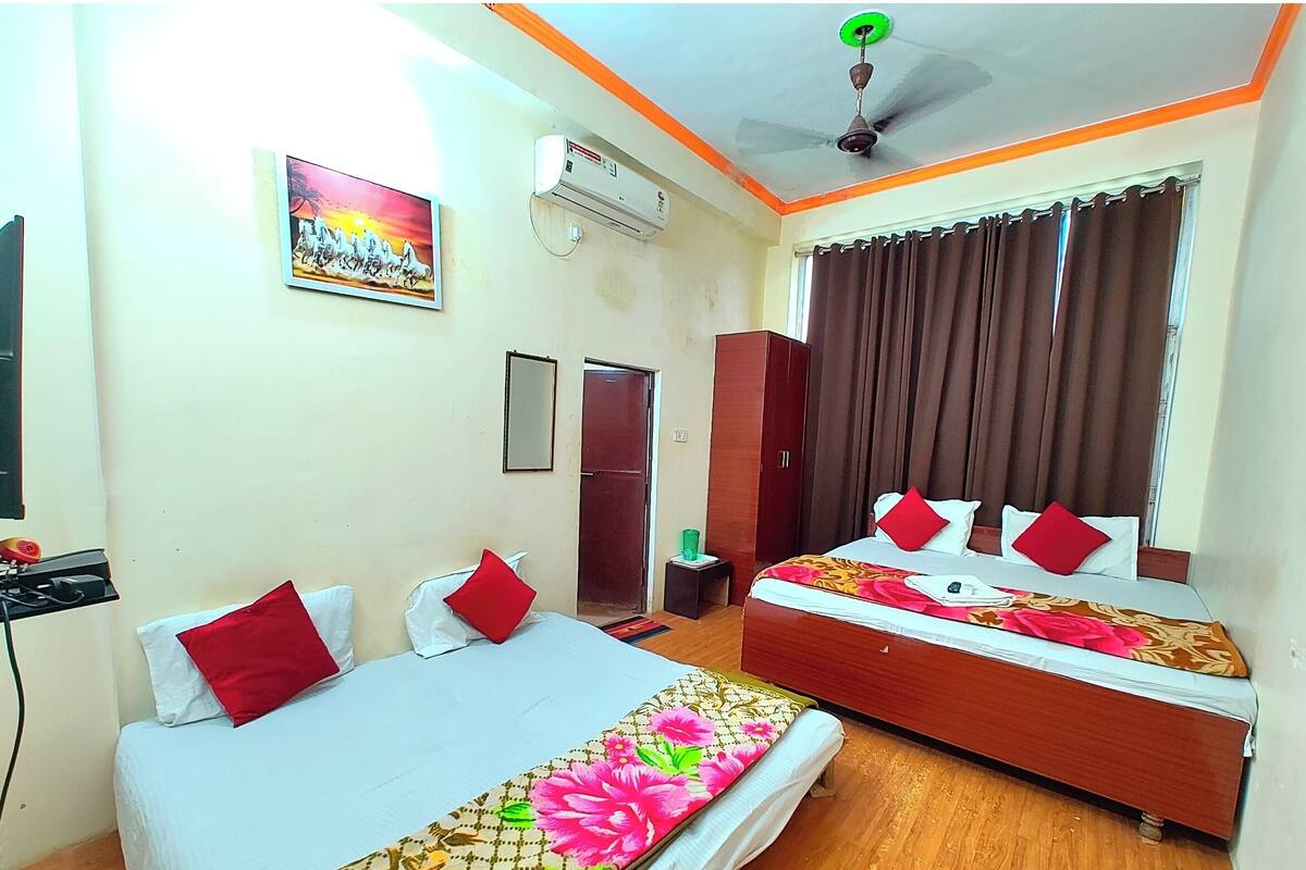 A hotel room with two beds, a ceiling fan, an air conditioning unit, a painting, a mirror, and a wardrobe.