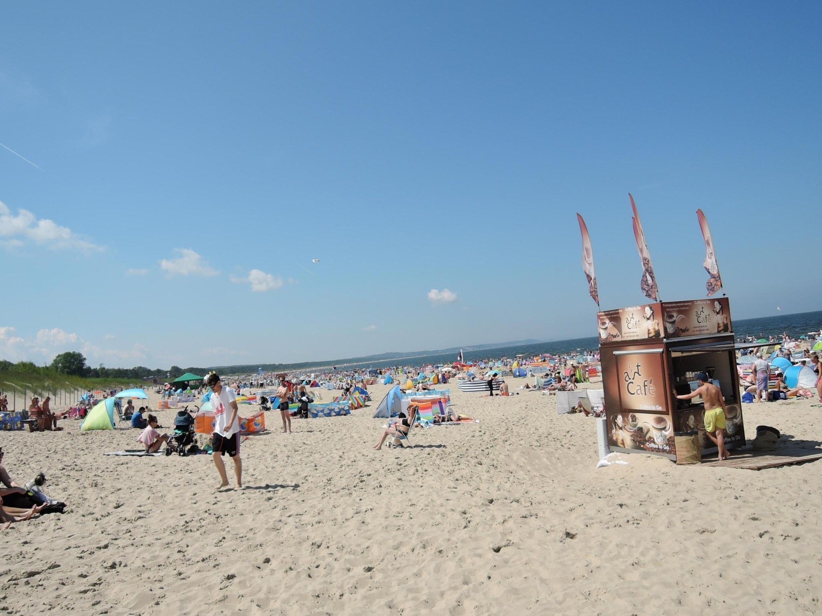 Una playa con gente, tiendas de campaña y un puesto de café.
