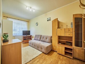 Een woonkamer met een bank, een houten kast, een tv-meubel en een plant.