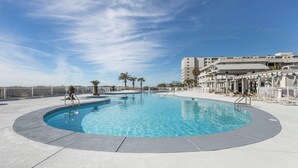A large, circular swimming pool with a clear blue center, surrounded by a white deck and palm trees. - Gulf Shores Plantation 2123 Fun & Games (Gulf Shores)