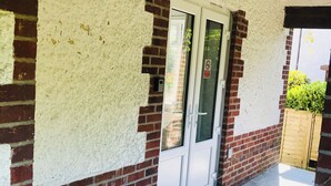 A building exterior with a white door, brick walls, and a concrete floor. - The studio (St Austell)