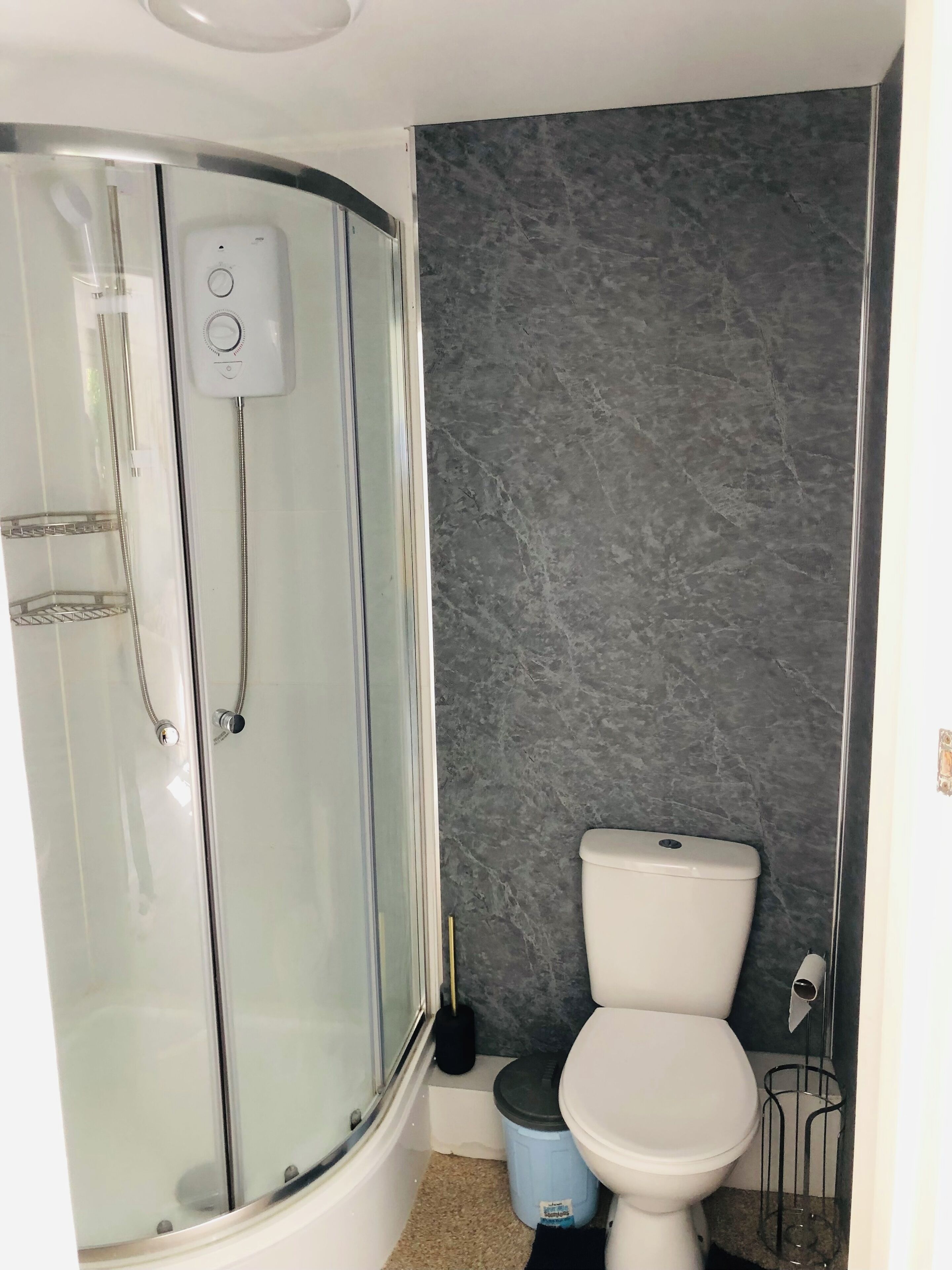 Um banheiro com chuveiro em box de vidro, vaso sanitário e parede de mármore.