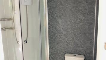 Um banheiro com chuveiro em box de vidro, vaso sanitário e parede de mármore.