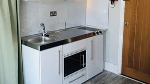 A compact kitchen with white cabinetry, a stainless steel sink, and a built-in oven. - The studio (St Austell)