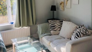 A living room with a glass coffee table, a beige sofa with patterned cushions, a black floor lamp, and framed floral artwork on the wall. - The studio (St Austell)