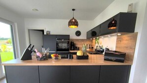 A modern kitchen with dark cabinetry, a wooden countertop, and a hanging pendant light. - Villa Vulkaneifel - relaxation & enjoyment (Darscheid)
