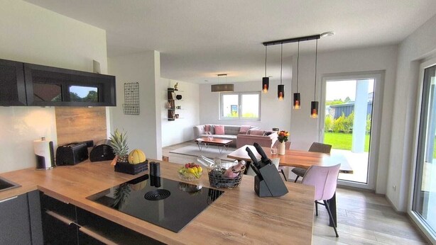 A modern kitchen with an island, a dining area with a table and chairs, and a living room with a sofa. - Villa Vulkaneifel - relaxation & enjoyment (Darscheid)