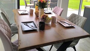A dining area with a wooden table, cushioned chairs, a vase with flowers, and a view of a green landscape through large windows. - Villa Vulkaneifel - relaxation & enjoyment (Darscheid)