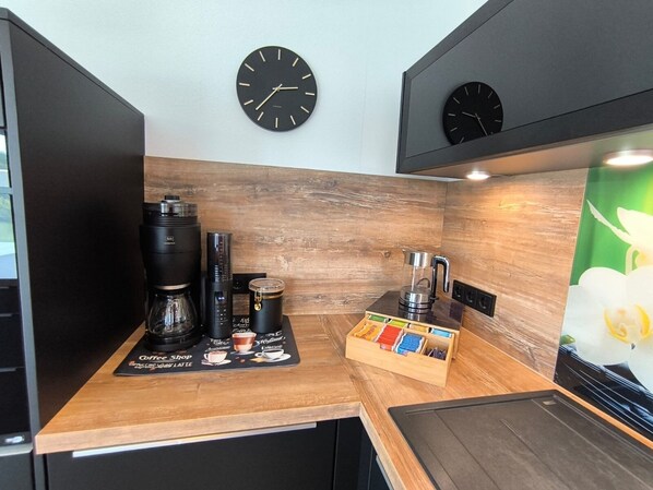 A modern kitchen with wooden accents, a coffee shop placemat, a coffee maker, a blender, and two wall clocks.