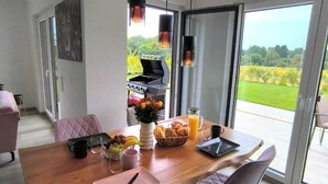 A dining area with a wooden table, chairs, and a grill outside the sliding glass door. - Villa Vulkaneifel - relaxation & enjoyment (Darscheid)