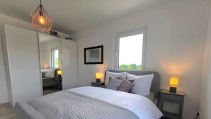 A bedroom with a large bed, bedside tables with lamps, a wardrobe, a mirror, and a window with natural light. - Villa Vulkaneifel - relaxation & enjoyment (Darscheid)
