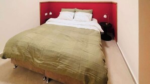 Una cama individual con cabecera roja, una manta verde y una almohada blanca.