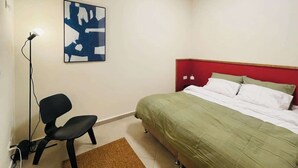 Un dormitorio con una cama, un escritorio, una silla, una lámpara y una obra de arte en la pared.